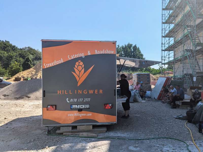 Heck eines Foodtrailers von Hillingwer Catering auf einer Baustelle mit Gerüst im Hintergrund