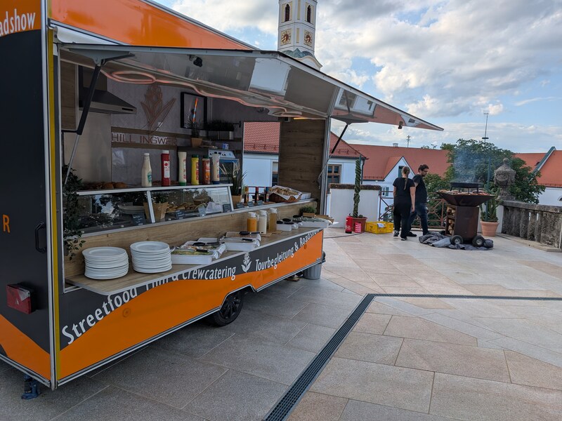 Foodtrailer mit Selbstbedienungstheke vor einer Kirche auf einem Stadtplatz