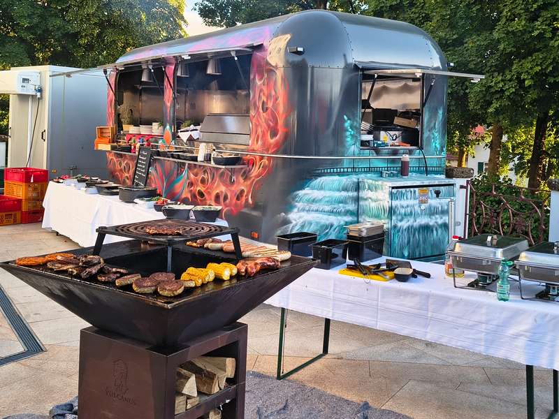 Foodtrailer mit Airbrush-Lackierung und Grill, davor ein gedecktes Buffet im Freien