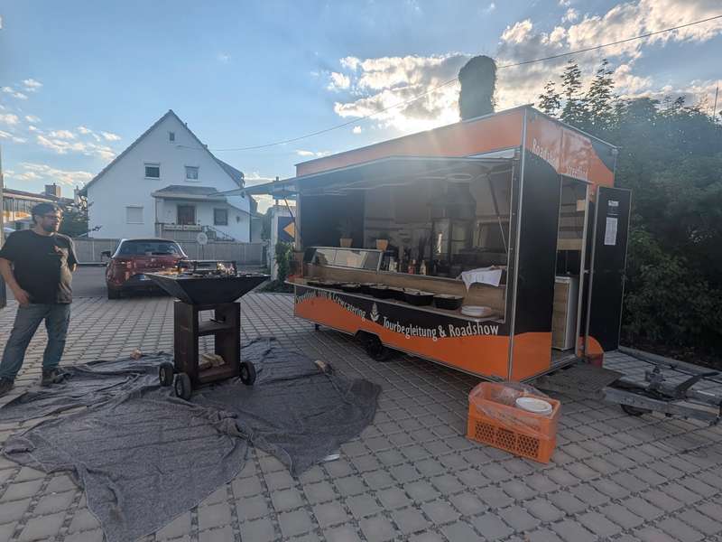 Foodtrailer und Feuerschale auf einem gepflasterten Hof, bereit für eine Firmenfeier im kleinen Kreis