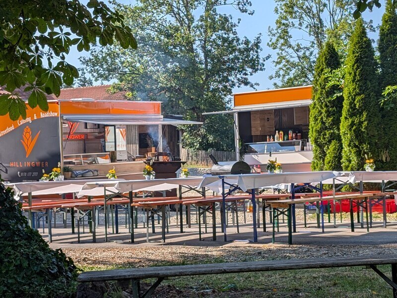 Zwei orange Foodtrailer und lange Biertischgarnituren im Freien, bereit für eine Party