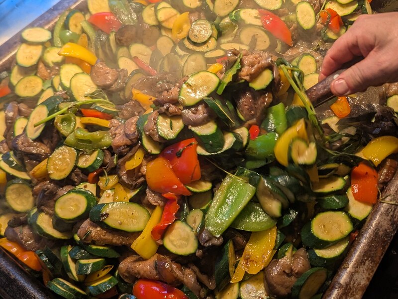 Zucchini, Paprika und Fleischstreifen in der Gemüsepfanne, eine Hand rührt mit der Zange um