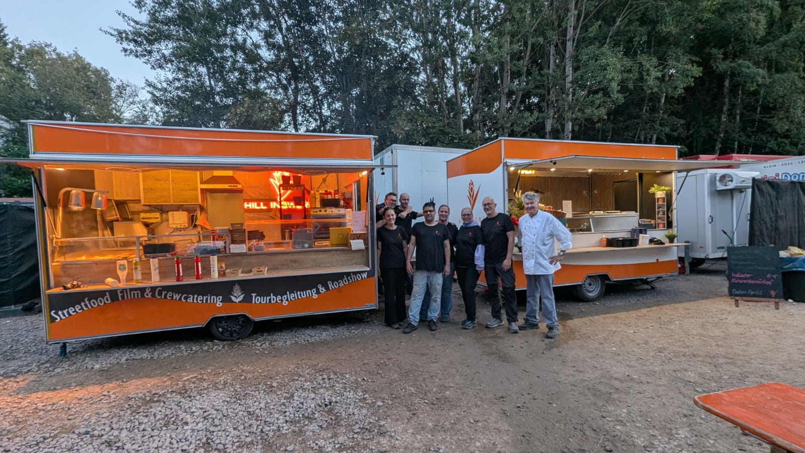 Das Hillingwer-Team steht abends zwischen zwei Foodtrailern auf einem Kiesplatz