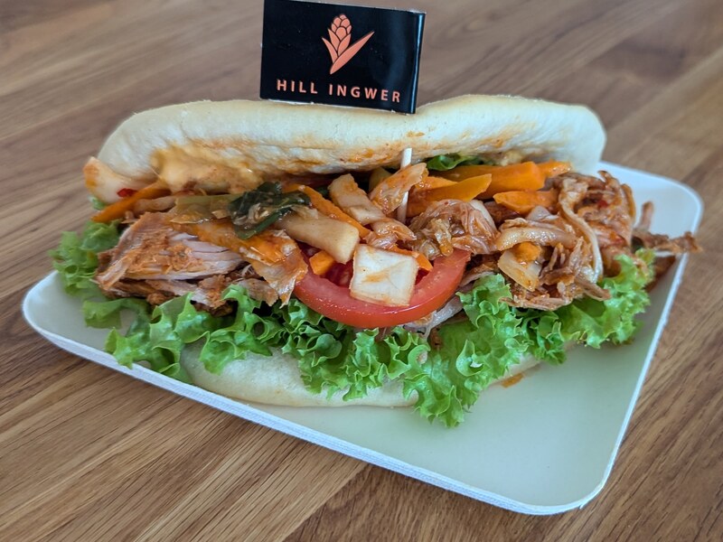 Pulled-Chicken-Sandwich mit Kimchi, Salat und Tomate auf einem Teller